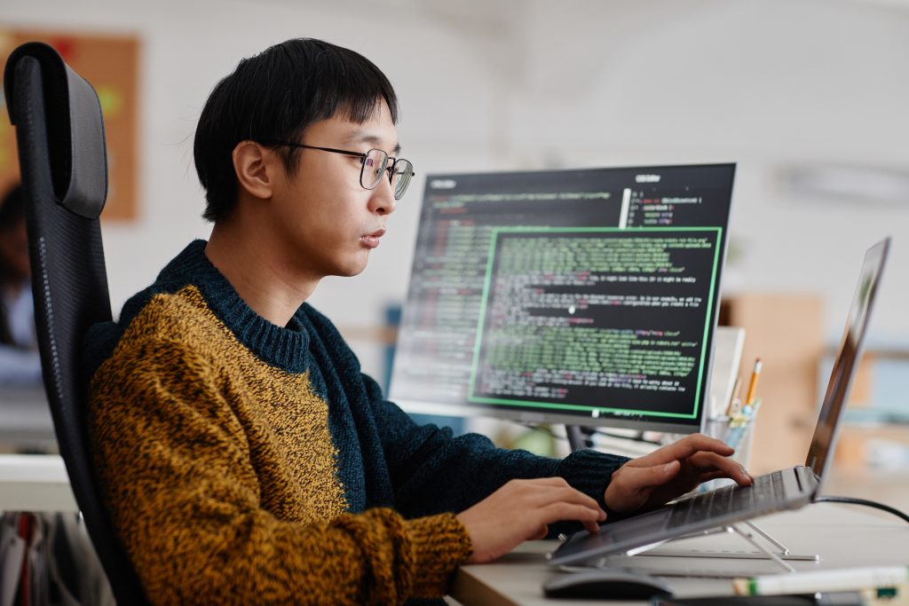 Vietnamese developer coding at a workstation with multiple screens, focusing on Full-Stack JavaScript development.